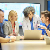 a mixed group of healthcare professional and business people meet around a conference table .