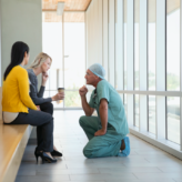 Clinician in scrubs kneeling in front of patient family to speak to them