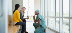 Clinician in scrubs kneeling in front of patient family to speak to them