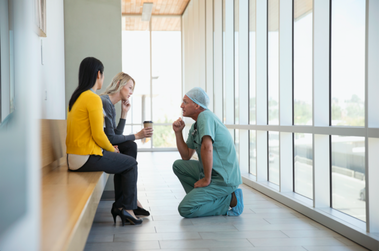 Clinician in scrubs kneeling in front of patient family to speak to them