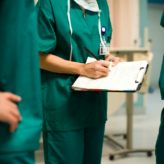 Three Doctors in Scrubs Writing on a Chart