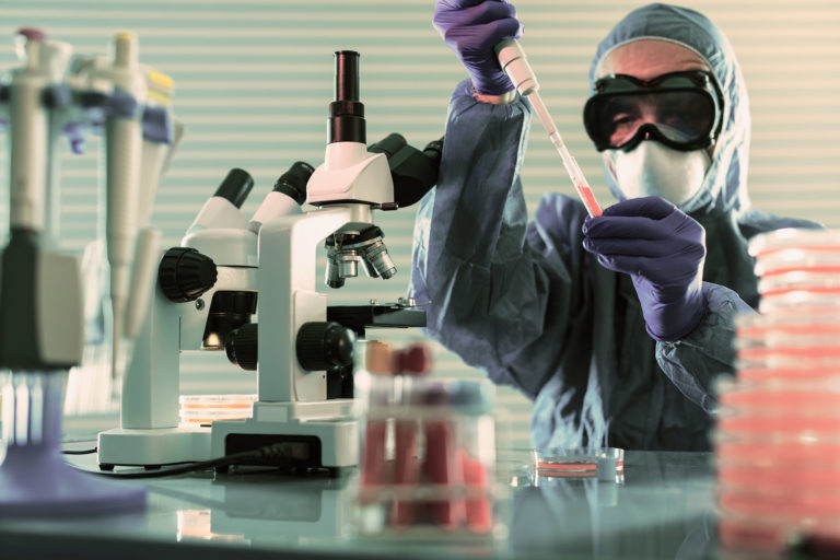 researcher in front of a microscope fills a vial with coronavirus vaccine